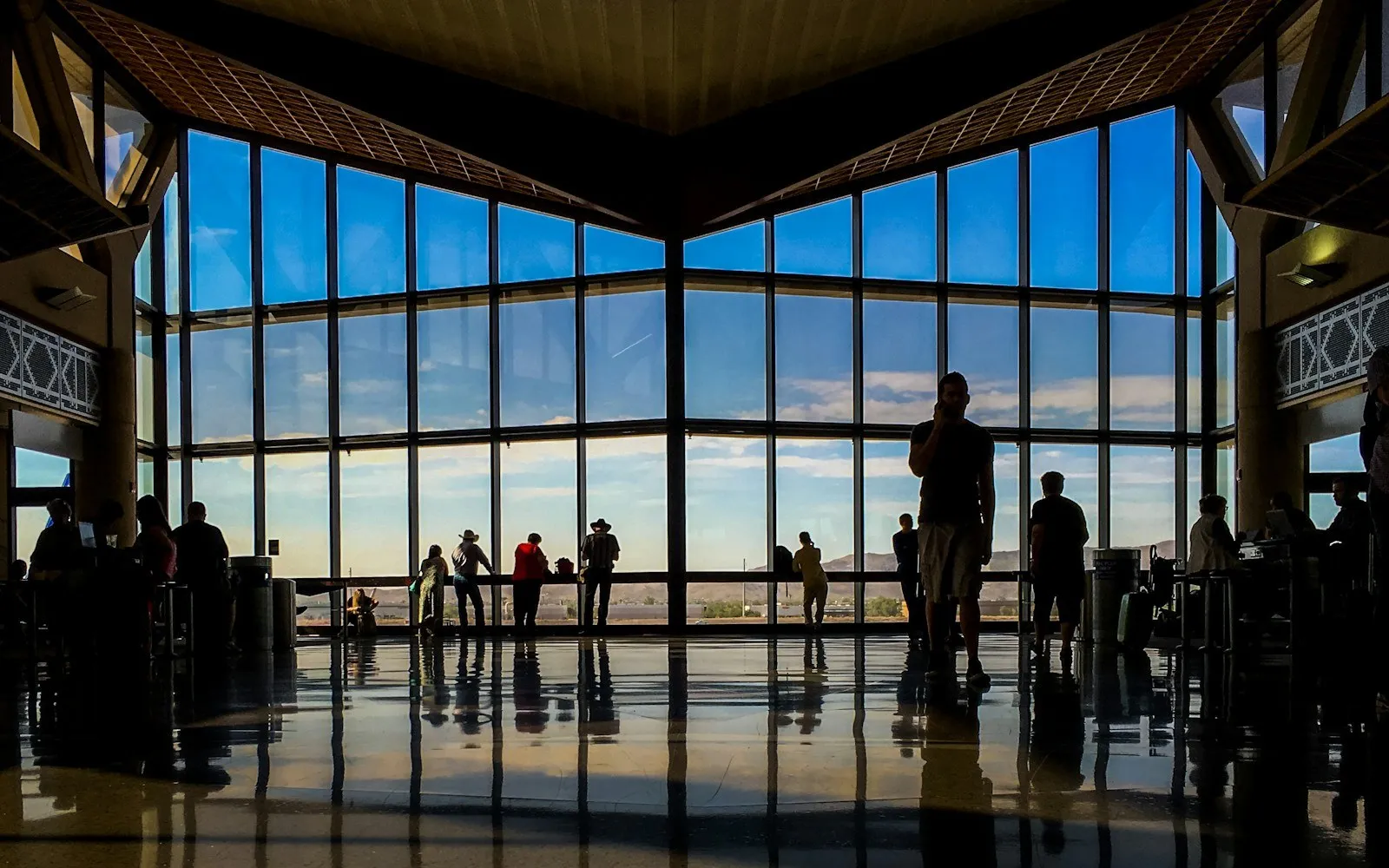 Travelers silhouetted against airport gate windows at sunset