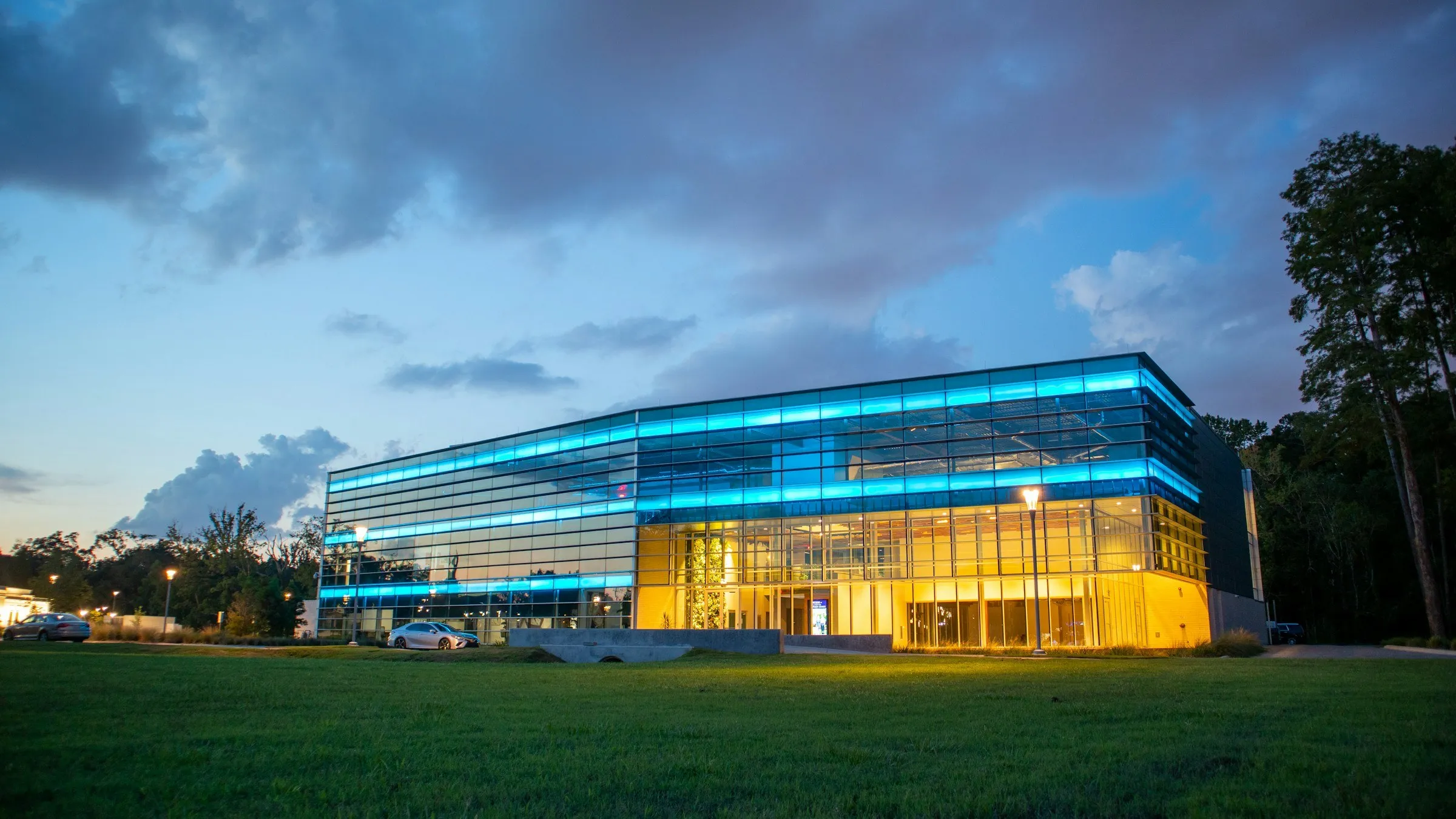 A glass commercial building lit blue and amber at dusk