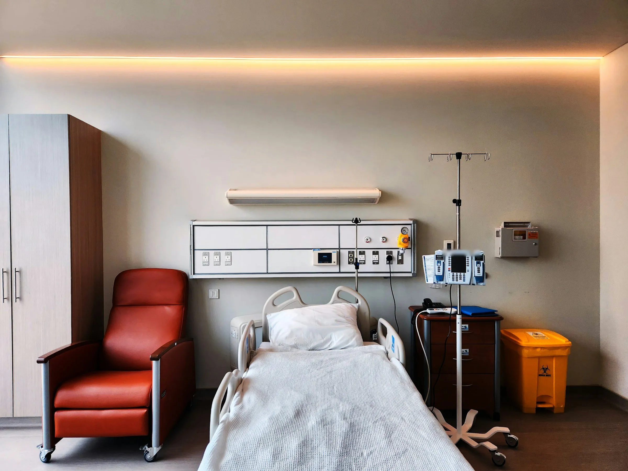 An empty hospital patient room with a bed, an IV pump and medical gas outlets on the wall
